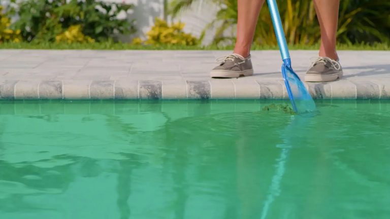 Technician skimming algae debris at the pool edge during a green pool cleanup in Metro Atlanta